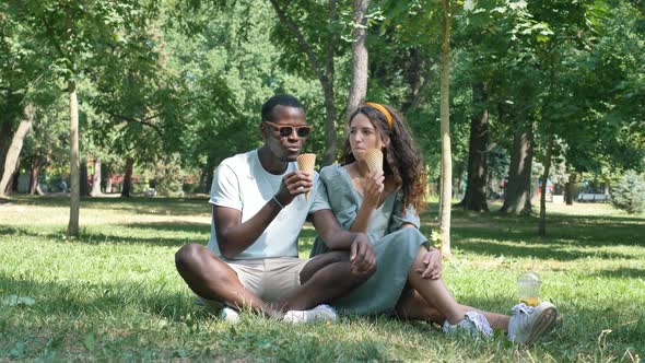 Black Man and Brunette Eat Organic Icecream on Grass Lawn