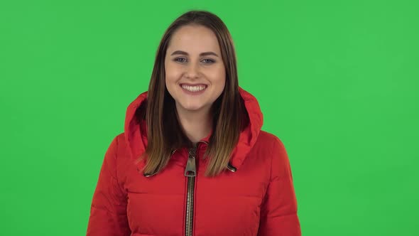 Portrait of Lovely Girl in a Red Down Jacket Is Smiling While Looking at Camera . Green Screen