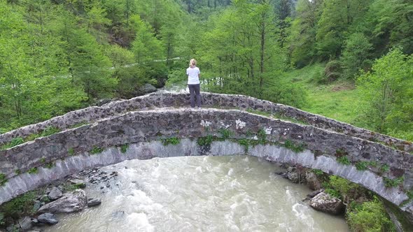 Yellow Hairy Woman Watching From Historic Stone Bridge in Forest Valley