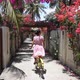 Cute Girl in Lovely Dress Riding Bicycle Through Majestic Tropical Magnificent Passage with Pink - VideoHive Item for Sale