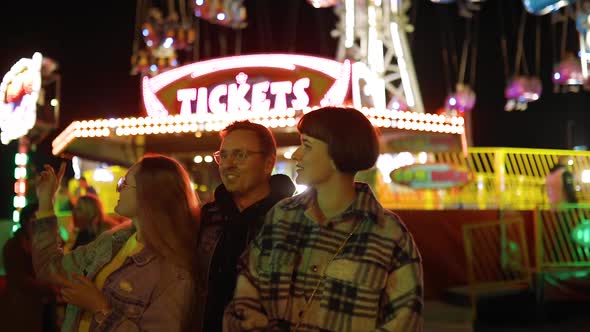Three Excited Friends Discuss at Which Attraction To Go Near Ticket Office at Amusement Park