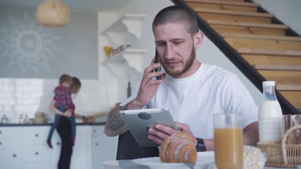 Young Brunette Man Hanging Up Phone, Talking To Blurred Wife and Daughter Standing at the Background