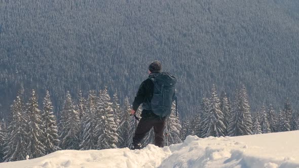 Successful Hiker with Backpack Walking on Snowy Mountain Hillside on Cold Winter Day