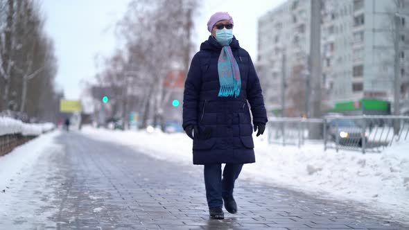 Elderly Woman in a Medical Face Mask Is Walking the Street