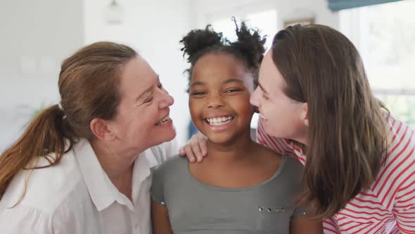 Portrait of happy caucasian lesbian couple and their african american daughter embracing and smiling