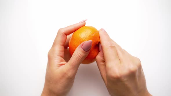 Woman cleans tangerine on the table