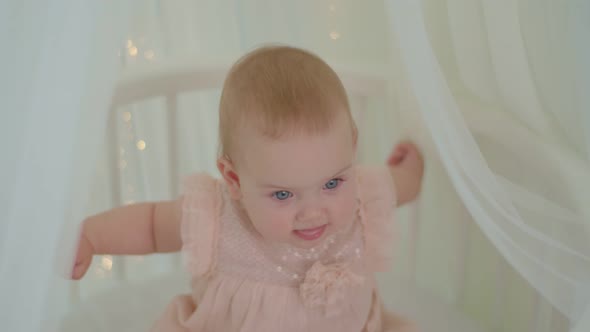 Close Up 10 Months Old Baby Girl with Blue Eyes Sitting in Bed with Canopy with Lights