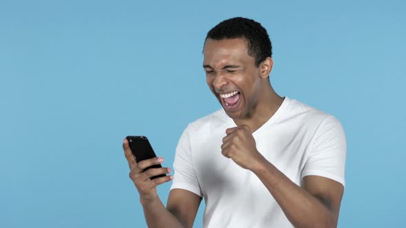 Young African Man Excited for Success While Using Smartphone