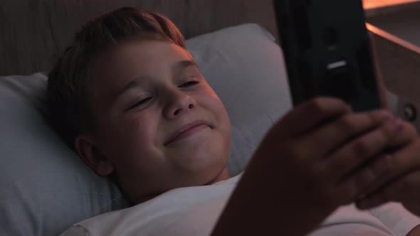 Happy Child Uses Phone While Lying in Bed Late at Night