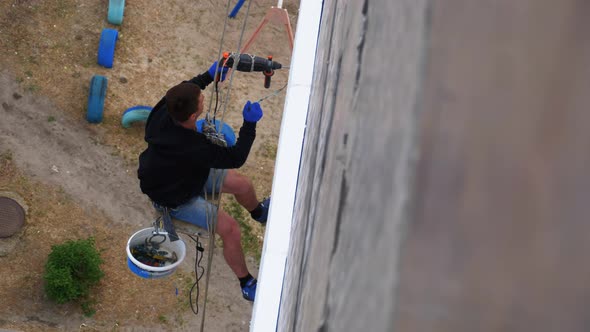 Industrial Climber Suspended on Ropes Insulates Facade with Styrofoam Near Wall