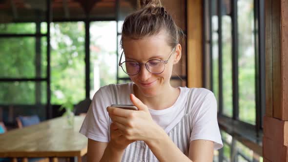 Adult woman in glasses browsing social media on smartphone 