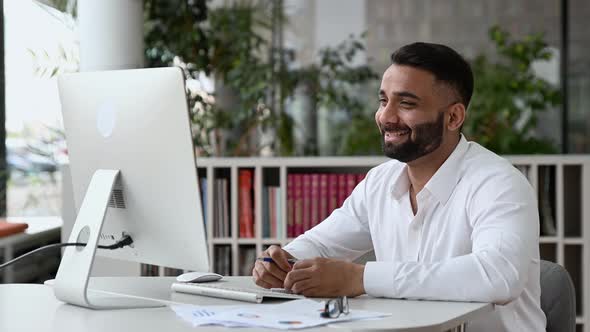 Friendly Confident Successful Indian Man Businessman or Mentor Sitting at His Desk Wearing a White