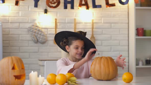 Cute Little Witch Sitting at Halloween Party With Jack Pumpkin Showing Thumbs-Up