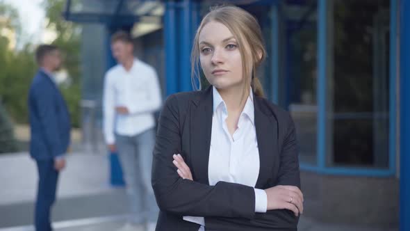 Portrait of Beautiful Young Businesswoman Standing Outdoors with Hands Crossed As Two Men Shaking