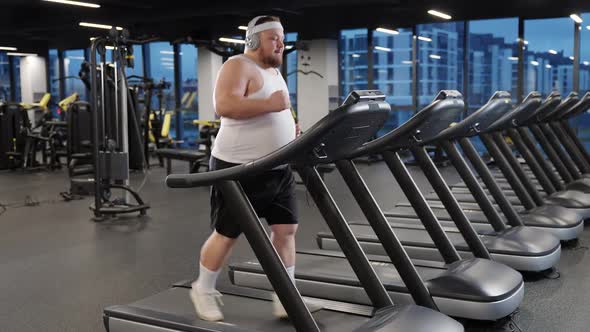 Fat Burning Overweight Man Run on a Treadmill and Listening to Music with Headphones Aerobic