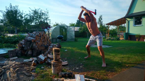 Strong Young Man Holding An Axe Splitting A Piece Of Firewood Outdoors In Lithuania. - Medium Shot