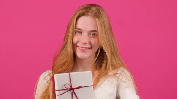 Red Haired Woman Offers Christmas Gift Box While Looking in Camera with a Smile