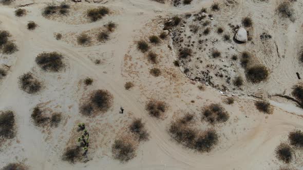 A Man leaves footprints in the desert as we watch him from a drone birds eye view walk through the b