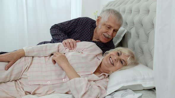 Senior Caucasian Grandparents Couple Lying in Bed at Home in Morning. Man Gently Whispering To Woman