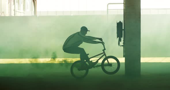 BMX rider in an empty warehouse using smoke grenade