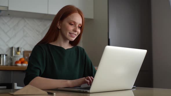 Smiling Young Redhead Woman Typing Online Social Media Message Using Laptop Computer Sitting at