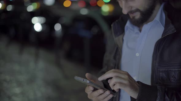 Handsome Smiling Man Working on Smartphone at Night