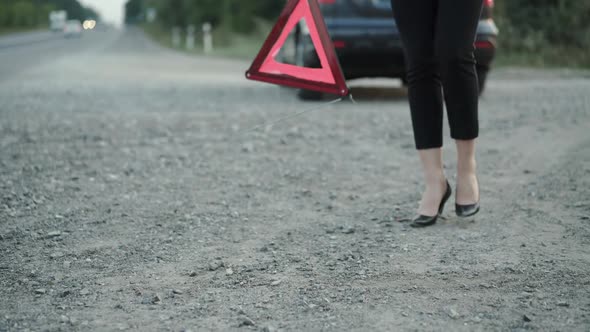 Low View of Woman with Broken Automobile Installing Red Triangle Sign on Road