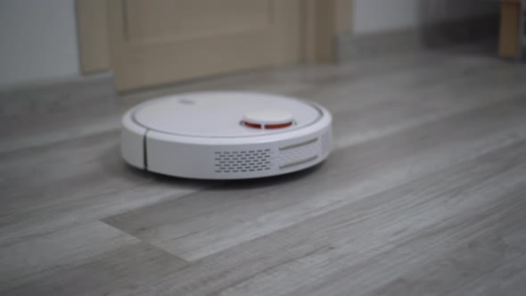 A White Robot Vacuum Cleaner Rides on a White Parquet Floor