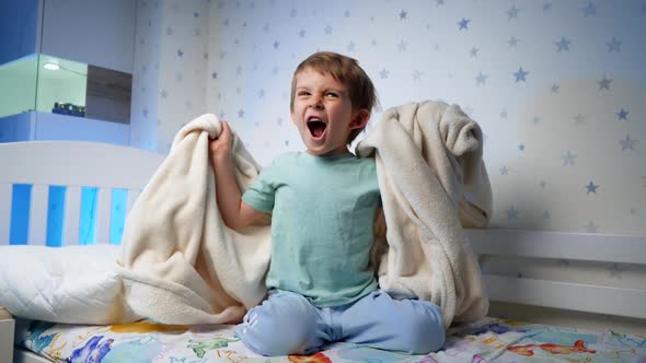 Funny Little Boy in Pajamas Laughing and Roaring While Sitting on Bed at Night