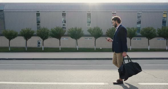 Business traveler walking near Airport with stylish Bag and browsing Smartphone.