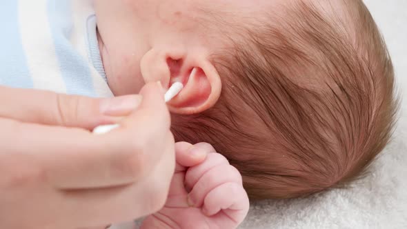 Closeup of Mother Using Cotton Swabs To Clean Little Baby's Ears From Ear Wax