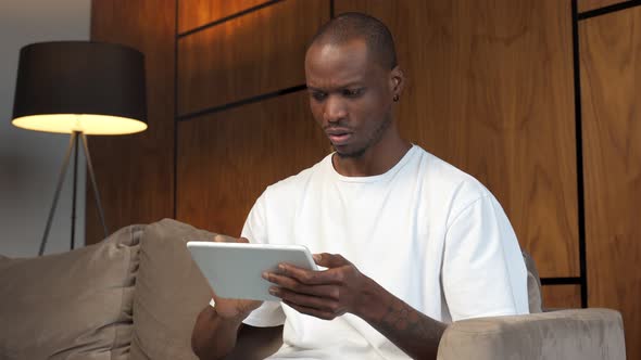 Young Black Man Using His Digital Tablet at Home Sitting on the Couch