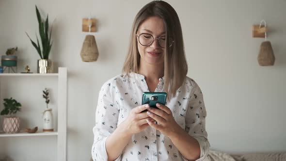 Woman with Eyeglasses Texting Message and Using Mobile Phone Smiling at Home
