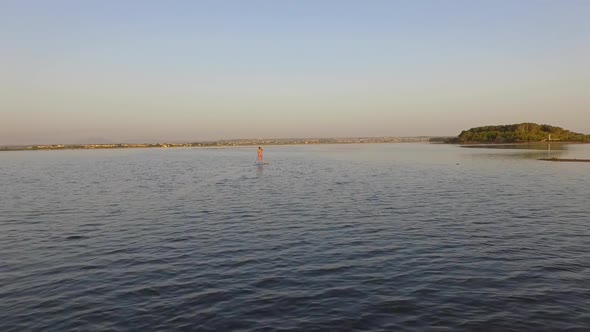 Aerial drone view of a woman SUP stand-up paddleboarding on a lake at sunset