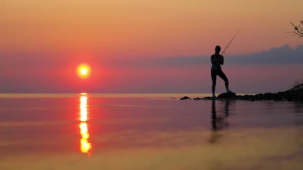 Woman Fishing on Fishing Rod Spinning at Sunset Background