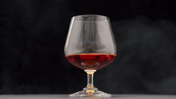 A Drop of Brandy Falls Into a Glass of Strong Alcohol on a Black Background