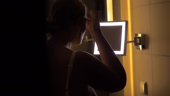 Woman looking in bathroom mirror after applying facial cream