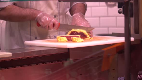 Closeup of chef cutting beef into slices with knife on cutting board