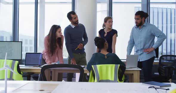 Diverse group of male and female architect colleagues gathered around a table and discussing