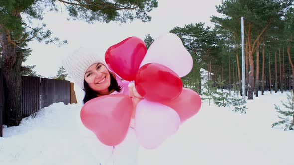 Happy woman throws up heart-shaped balloons outdoor in winter with snow