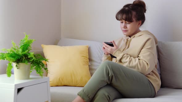 Young Blonde Woman Sitting with Smartphone on Sofa