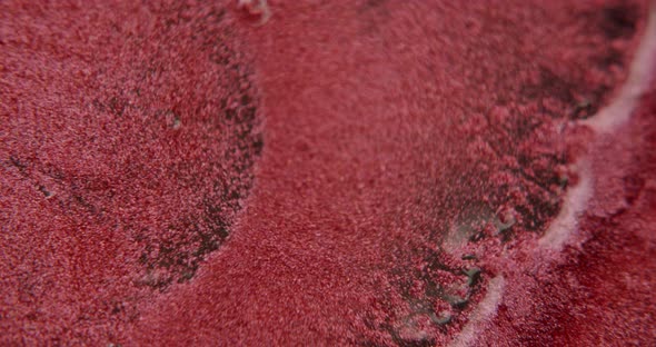 Water squirting onto a red sandlike surface. Particles get mixed with the water.