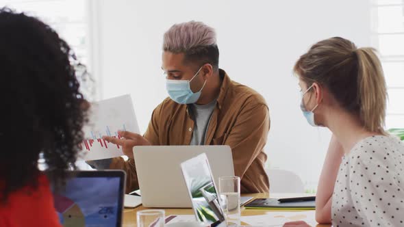 Man wearing face mask showing a document to his colleagues at office