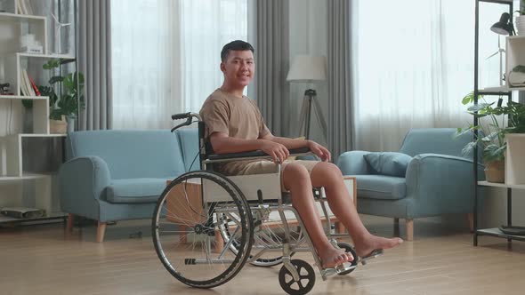 Young Asian Boy Sitting In A Wheelchair Smiling And Looking At Camera In Living Room