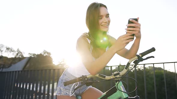 Smiling Girl in with Long Hair Sits on Bicycle and Something Watching in Smartphone App