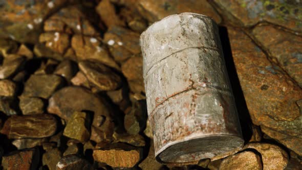 Rusty Destroyed Metal Barrel on Beach Rocks