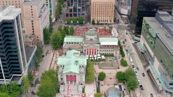 Wide aerial reveal of a popular political rally in a major city downtown core. Protesters wearing or