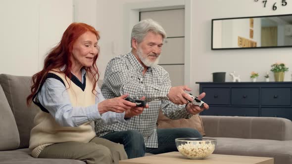 Cheerful Senior Couple 5060 Years Old Playing a Video Game at Home Sitting on the Couch