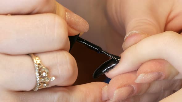 A Manicurist Paints a Long Extended Nail for a Client with Black Nail Polish