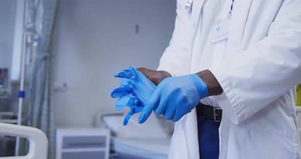 Midsection of african american male doctor wearing latex gloves in hospital patient room